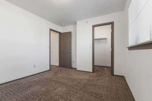 A room with brown carpet and white walls with two doors.
