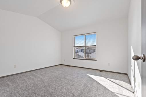 A room with a carpeted floor and a window showing a house view.
