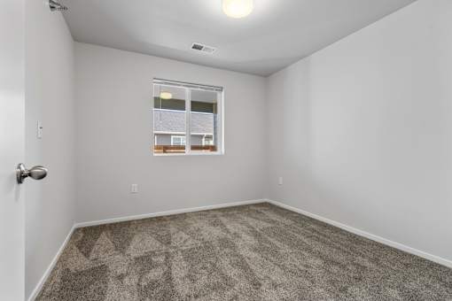 A room with a carpeted floor and a window showing a view of a building.