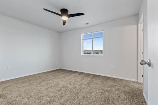 A room with a ceiling fan and a window showing a view of a building.