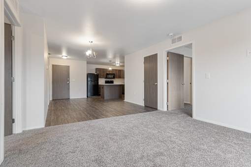 A spacious living room with a grey carpet and a kitchen area in the background.