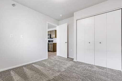 A room with white walls and a carpeted floor with a white door on the right.