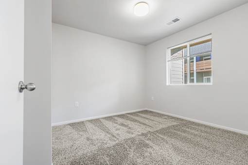 A room with a carpeted floor and a window showing a building outside.