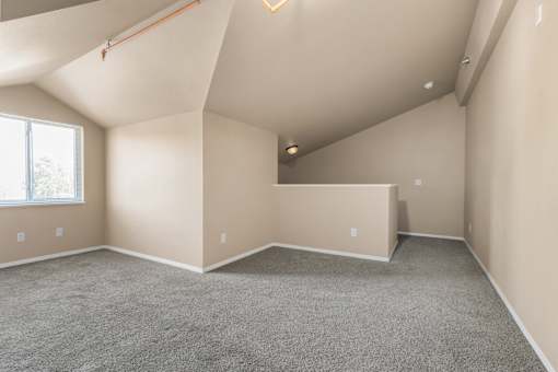 A spacious room with a window and a grey carpet.