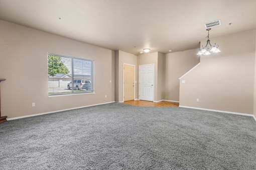 A spacious room with a grey carpet and a large window.