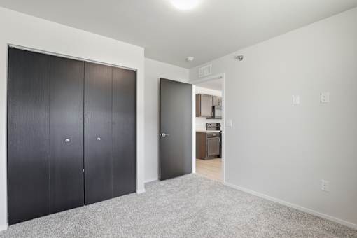 A room with a white wall and a carpeted floor with a black door on the left and a white door on the right.