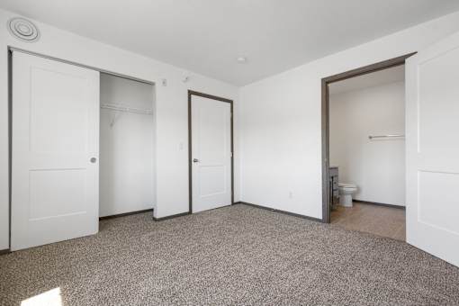 A room with white walls and a carpeted floor with four doors.