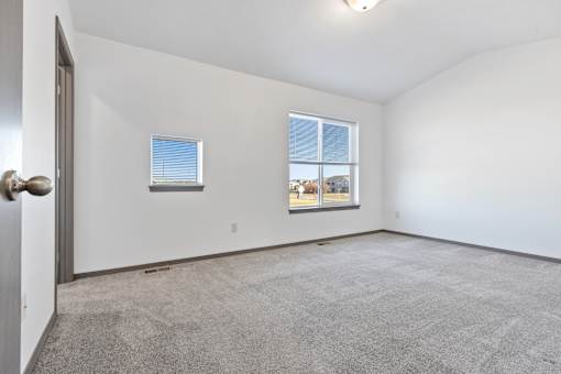 A room with a carpeted floor and two windows.