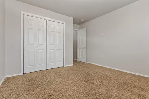 A room with carpeted floor and white walls with a white door and a white wardrobe with four doors.
