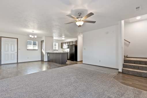 A spacious living room with a grey carpet and a ceiling fan.