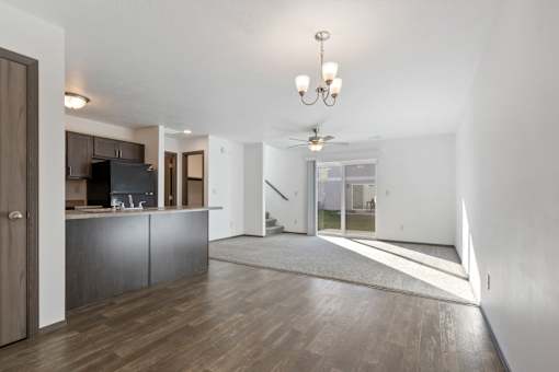 A spacious living room with a kitchen area and a ceiling fan.