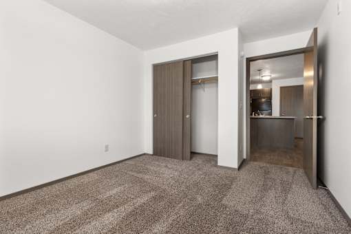 A room with a carpeted floor and a doorway leading to a kitchen.