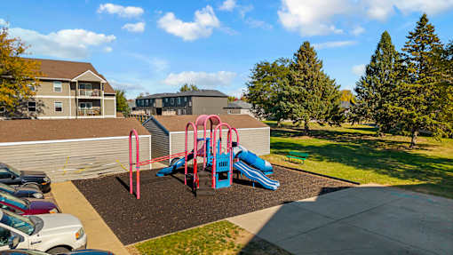 A playground with a slide and swings in a parking lot.