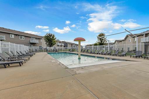 A swimming pool surrounded by lounge chairs and apartment buildings.