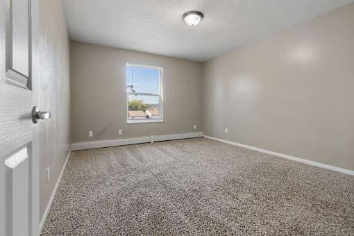 A room with a carpeted floor and a window showing a view of a building outside.