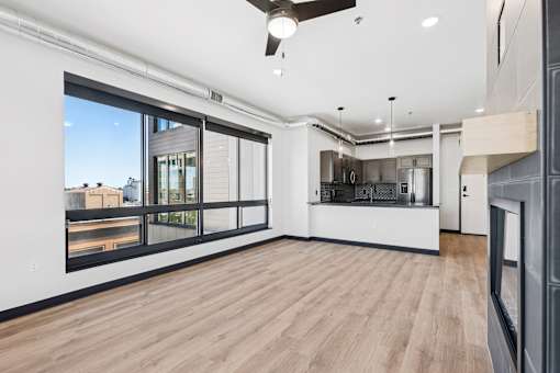 A spacious room with a ceiling fan and a view of the city through the windows.