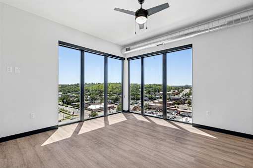 A room with a ceiling fan and large windows overlooking a cityscape.