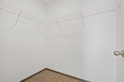 A white wall with a brown carpet and a silver door handle.