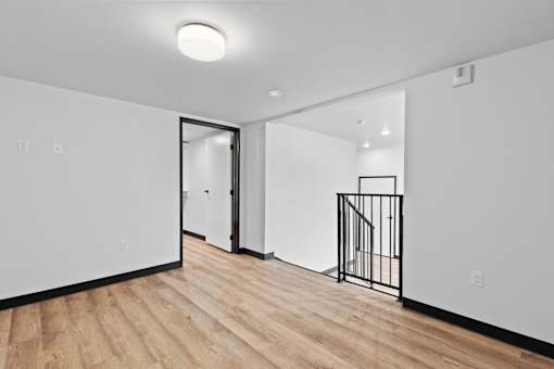 A room with a wooden floor and a white wall with a doorway leading to another room.