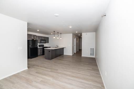an empty living room and kitchen with white walls and wood flooring