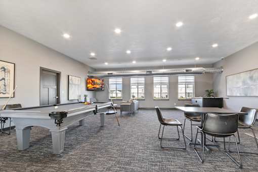 A room with a pool table, chairs, and a TV.