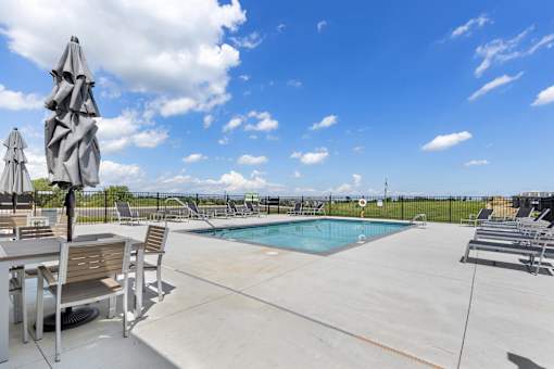 A pool area with a table and chairs and a blue pool.