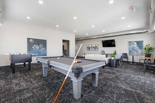 A pool table in a room with a chair and a plant.