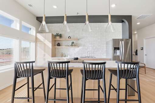 A kitchen with a white tile backsplash and a bar area with four chairs.