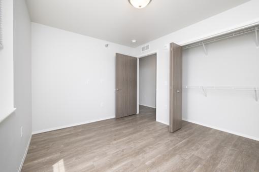 A room with a wooden floor and a white wall with a door and a closet.