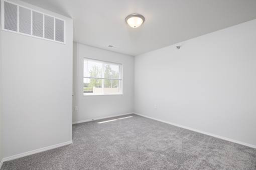 A room with a grey carpet and a window.