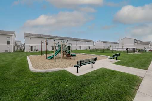 A playground with a green slide and two benches.