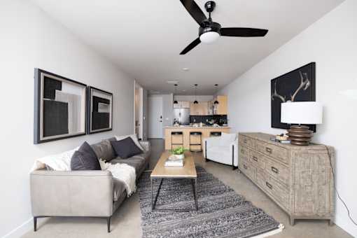 A living room with a grey couch and a black ceiling fan.