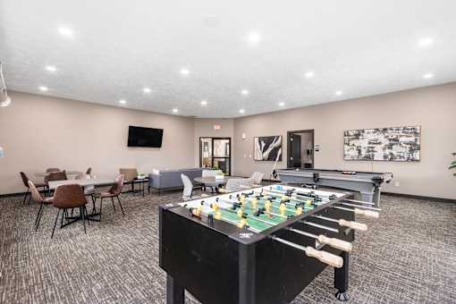 A foosball table is in the middle of a room with chairs and a TV.