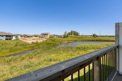 A wooden deck overlooks a grassy field with a river and houses in the distance.