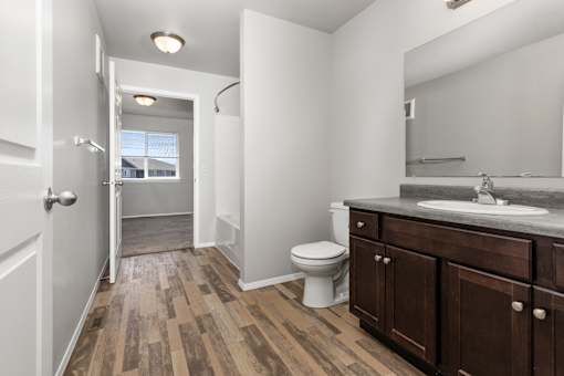 A bathroom with a toilet, sink, and wooden floors.