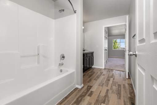 A white bathroom with a wooden floor and a white tub.