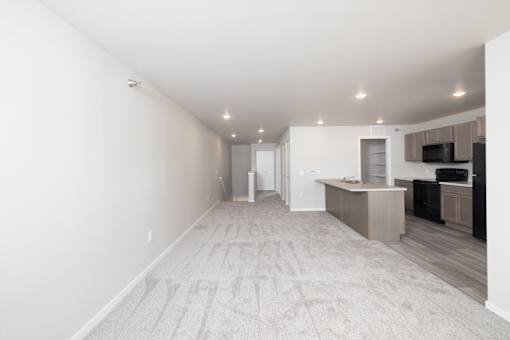 A spacious room with a carpeted floor and a kitchen area in the background.