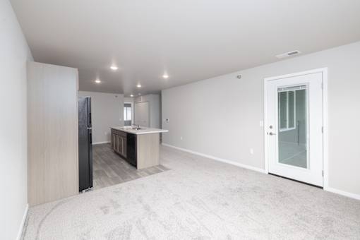 A spacious, empty room with a carpeted floor and a door leading to a bathroom.