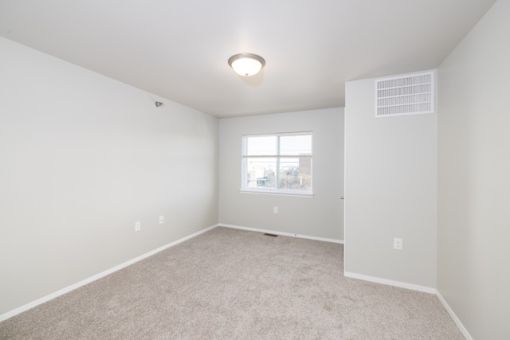 A spacious, empty room with a window and carpeted floor.
