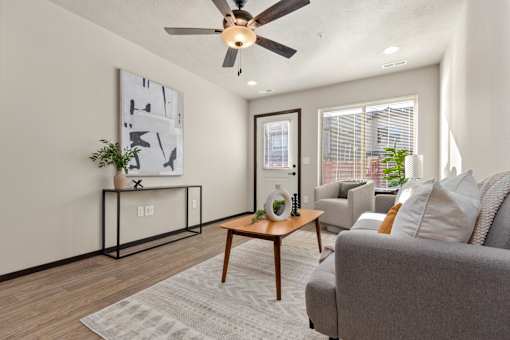 A living room with a grey couch, a wooden table, and a ceiling fan.