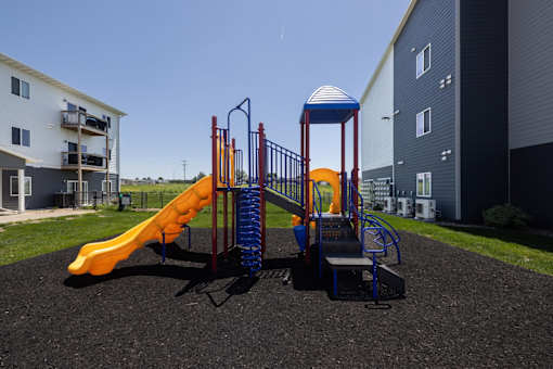 A playground with a yellow slide and a blue and red structure.