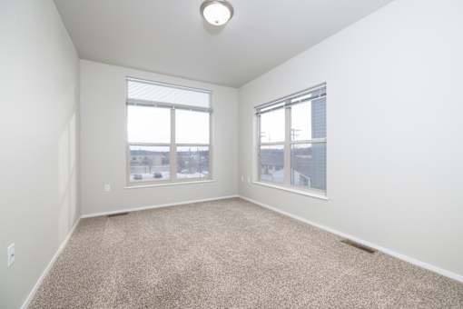 A room with a carpeted floor and two windows.
