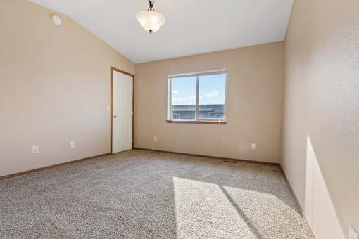A room with a carpeted floor, a window, and a door.
