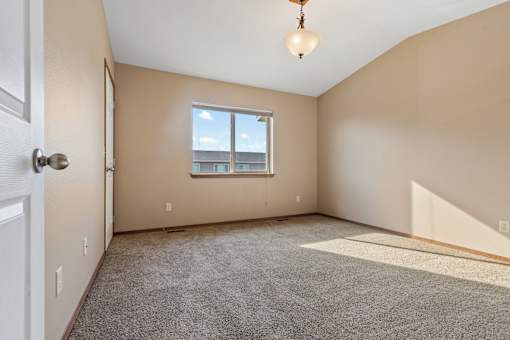A room with a carpeted floor, a window, and a door.