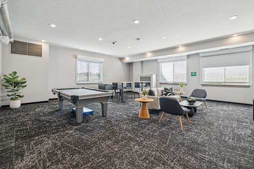 A room with a pool table, chairs, and a potted plant.