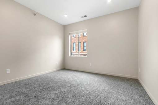 A room with a window and a grey carpet.