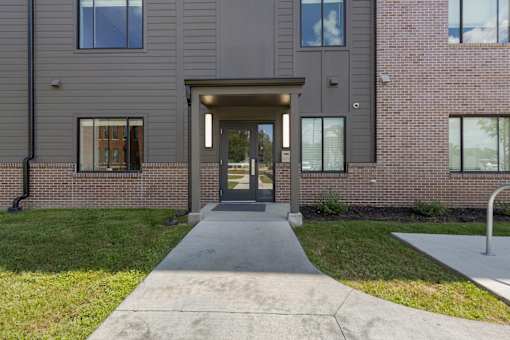 A building with a grey front and a concrete walkway leading to the entrance.