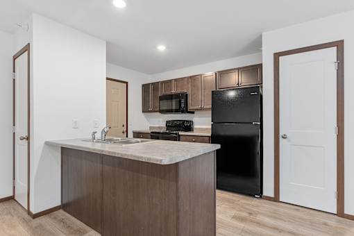 A kitchen with a black refrigerator and brown cabinets.