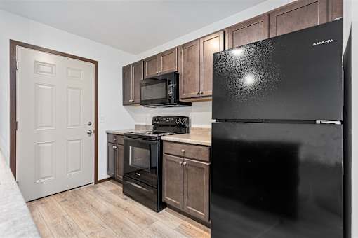 A black fridge in a kitchen with wooden cabinets and a microwave.