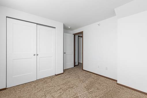A room with carpeted floor and white walls with a white closet and a door.